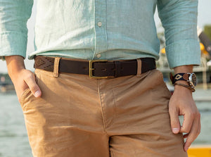 The LA MATERA - CASTANO POLO BELT by LA MATERA, featuring a dark brown leather embossed geometric design and brass buckle, is handcrafted in Argentina and coiled neatly against a plain white background.