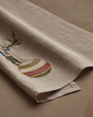 A beige linen DECK THE HALLS FOX LINEN TEA TOWEL embroidered with a fox holding a large, striped Christmas ornament, perfect for vintage Christmas kitchen decor.