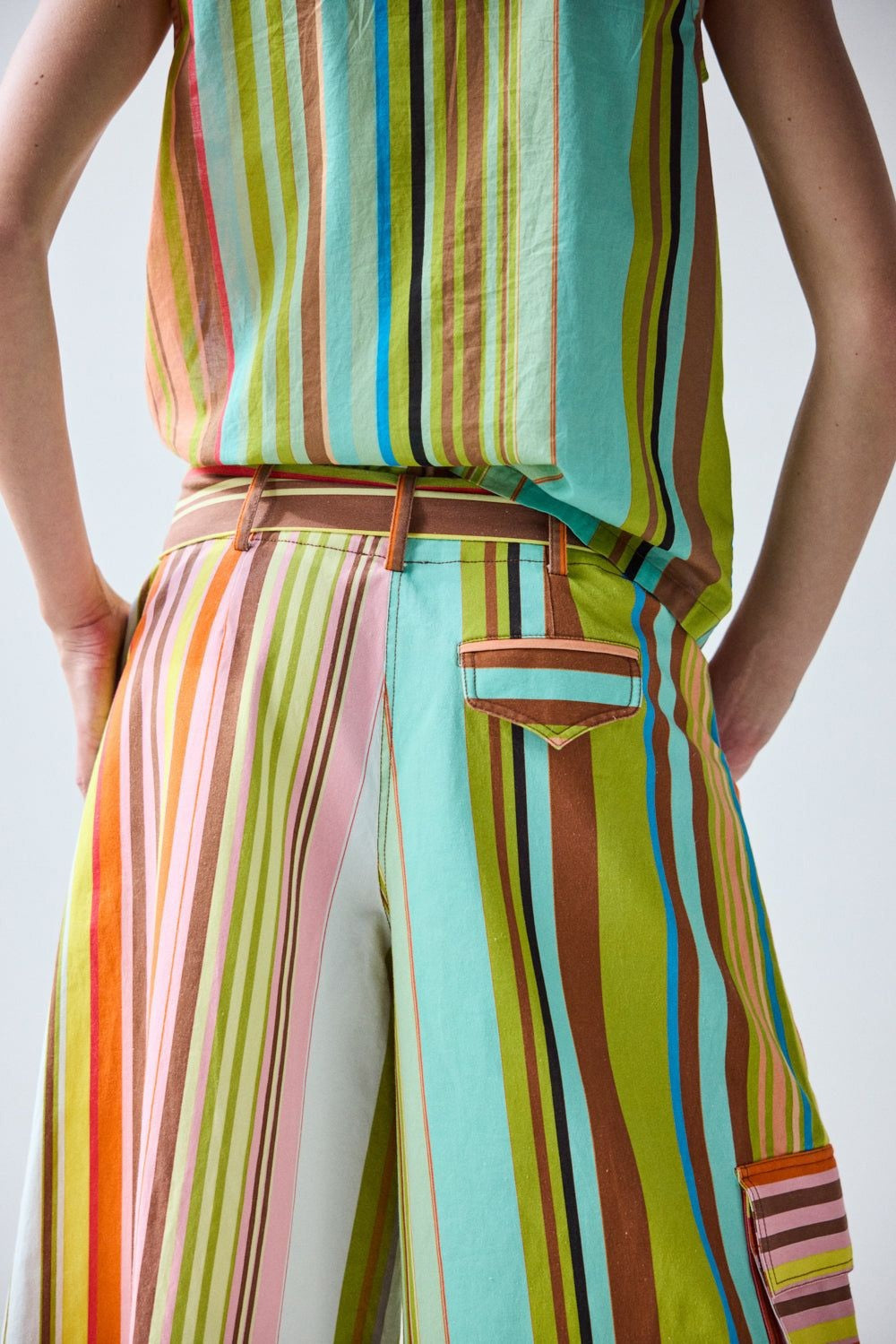 A person, seen from the back with hands on hips, wears the HOPE FOR FLOWERS - CROPPED PANT IN COMBO STRIPES: a colorful, striped matching set featuring wide leg cropped pants by HOPE FOR FLOWERS.
