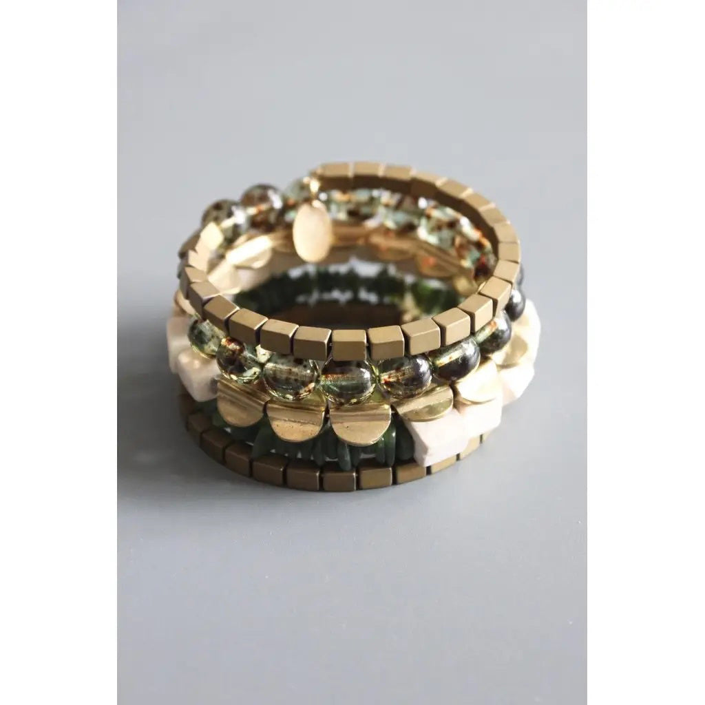 The DAVID AUBREY ATHENA HEMATITE GLASS AGATE JADE WRAP BRACELET, by DAVID AUBREY, features metallic gold square beads, transparent and ivory geometric accents—an elegant Mother&#39;s Day gift displayed on a gray background.