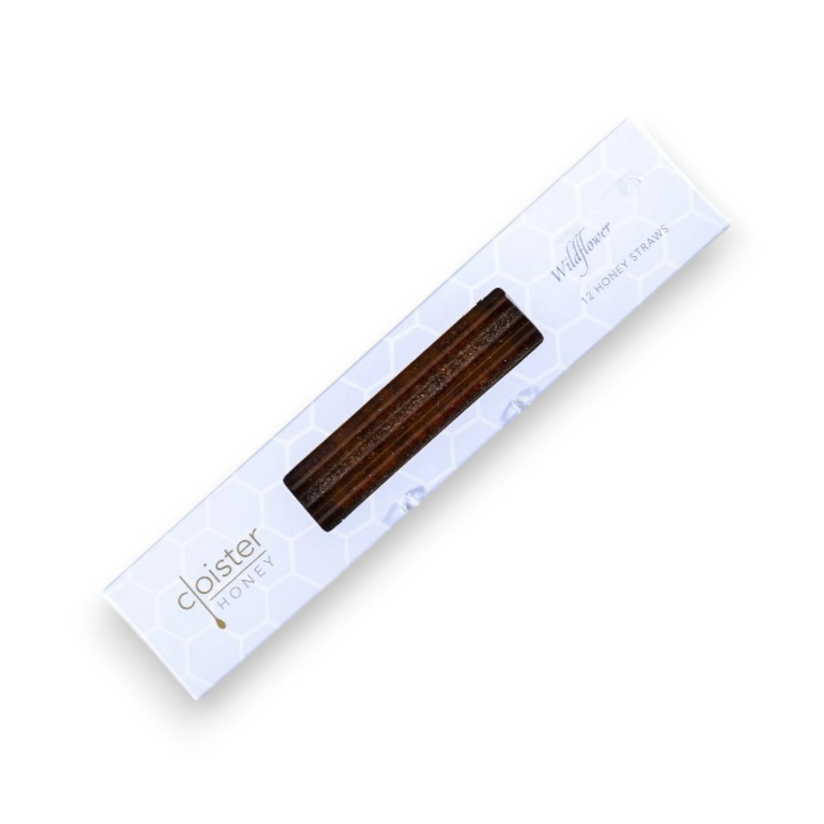 A floral teacup filled with tea sits on a square blue plate with two rectangular biscuits and an open Cloister Honey - Wildflower Honey Straw. A box labeled "Artisan Honey" and a jar containing more Wildflower Honey Straws are beside the plate on a rustic wooden surface with a grassy background.