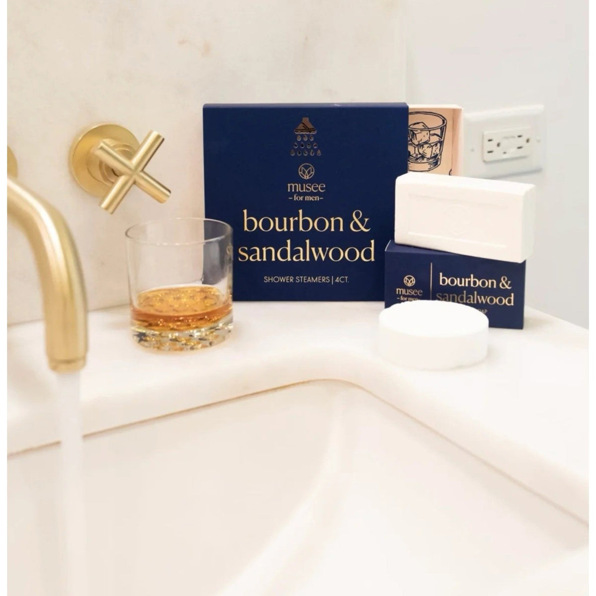 A rectangular white bar of MUSEE - BOURBON & SANDALWOOD BAR SOAP, known for its moisturizing properties, rests partially atop a blue box labeled with the product name and brand “MUSEE,” featuring a circular logo on both the soap and the packaging.