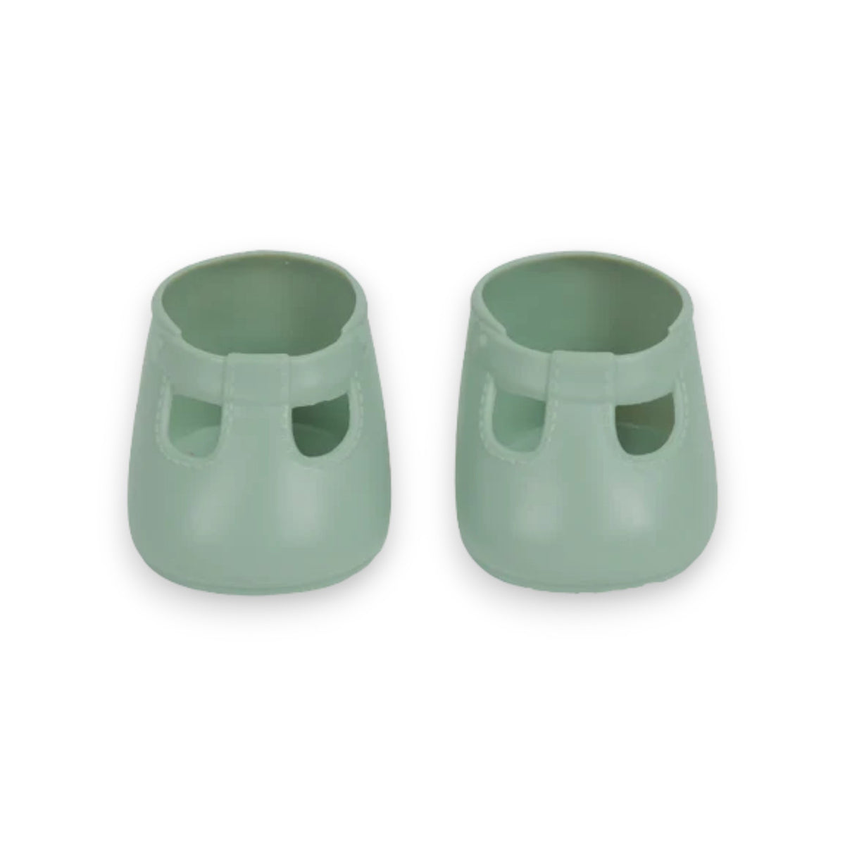 A close-up of a baby wearing OLLI ELLA USA DINKUM DOLL SHOES in Mallow Pink and white socks. The baby is seated on a soft, pale pink textured blanket, dressed in light brown clothing. Only the lower half of the baby's body is visible.