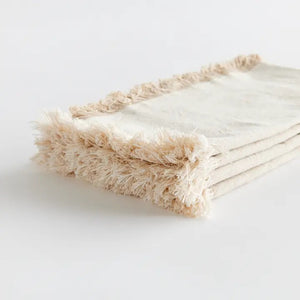 The NAPA HOME AND GARDEN - AURA Dinner Napkin in taupe is a square cotton napkin with fringed edges, neatly folded and set on a white background. Machine washable for easy care.