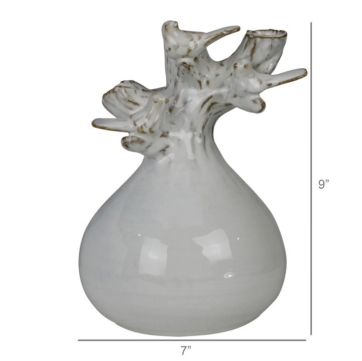 The HOMART CERAMIC VASE WITH BRANCH AND BIRD features white flowers and branches, set on a wooden surface with framed bird art and a woven basket against a light gray textured wall for a cozy touch.