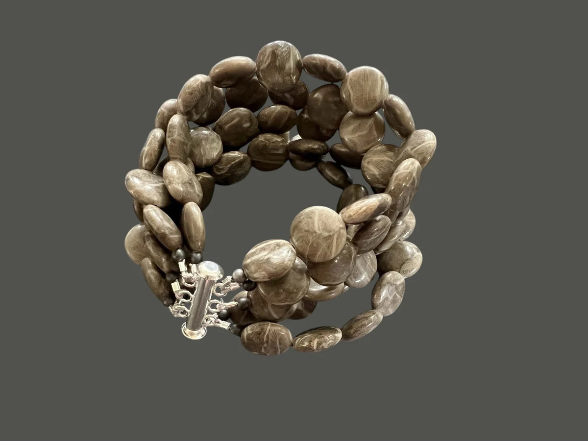 The ANN LIGHTFOOT Brown Jasper Coin Five Strand Bracelet features polished, oval brown jasper beads and a stainless steel clasp, shown on a plain gray background.