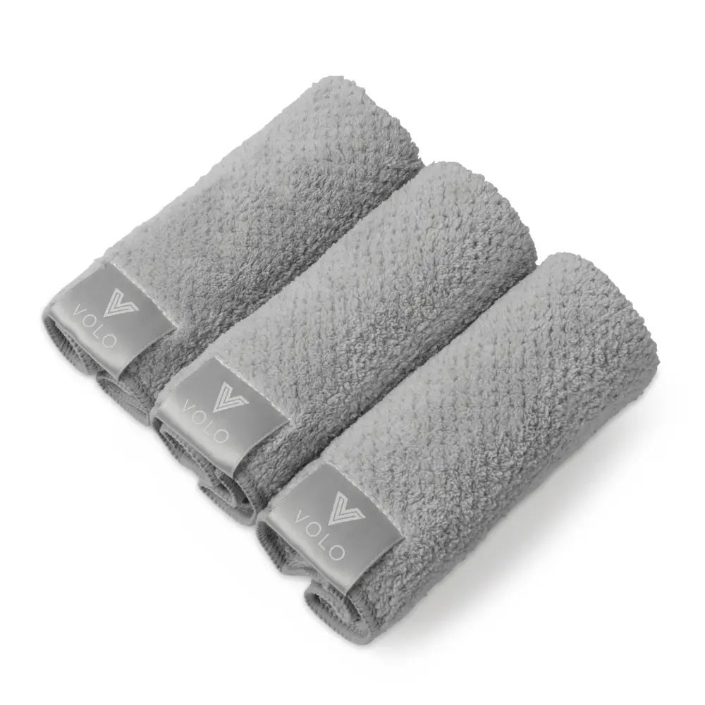 Three VOLO BEAUTY Face Towels from the Pack of 3 are rolled side by side on a white background, each showing a gray tag with the white logo and text, accentuating their luxury Nanoweave fabric.