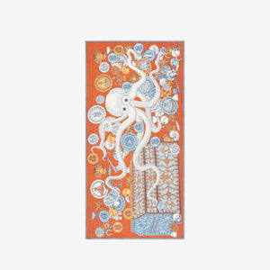 A woman with light skin and brown hair tied back wears a black outfit and the INOUI Editons Octopus Scarf in orange by INOUI, featuring intricate hand-printed patterns in orange, blue, and white draped over her shoulders.