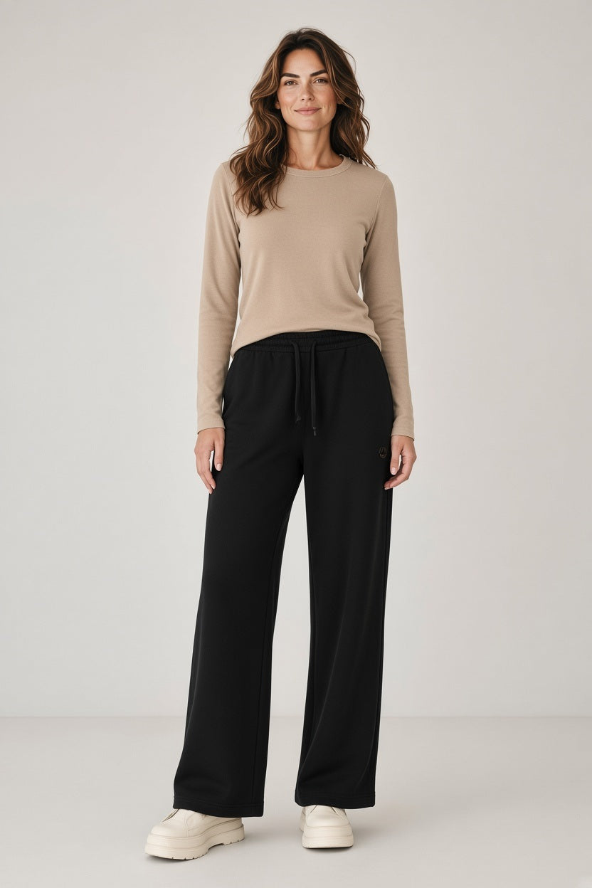 A woman wears a long-sleeved beige top tucked into black SAVE THE DUCK - IZUMI PULL ON DRAWSTRING WIDELEG PANT and chunky white platform shoes.