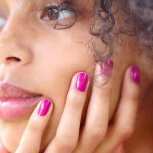A close-up of MANUCURIST - GREEN™ NAIL POLISH IN ARMERIA by MANUCURIST INC being spread with a brush on a smooth surface, showcasing its vibrant pinky mauve shade, glossy texture, and distinctive curved brushstroke.