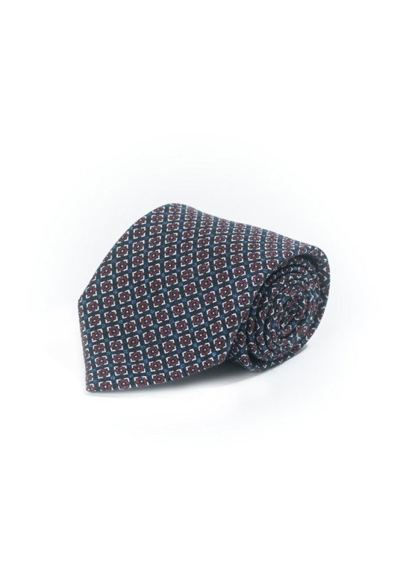 The EDWARD ARMAH - NAVY NEAT SILK TIE by EDWARD ARMAH features a rolled-up design in dark navy silk with a repeating geometric pattern in red, white, and blue on a white background.