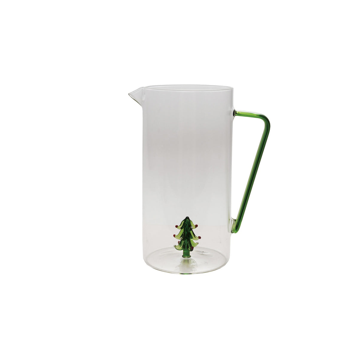 A CREATIVE COOP GLASS PITCHER WITH HOLIDAY TREE sits on a wooden surface with a green-stemmed glass holding snowy holiday trees beside it, set against a light background.