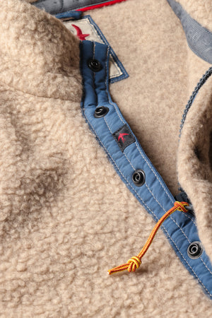 A person wearing the RELWEN Wooly Shag Snap-Zip in Dark Biscuit over a blue plaid shirt and green pants, with one hand in their pocket and a brown leather item partially visible at their waist.