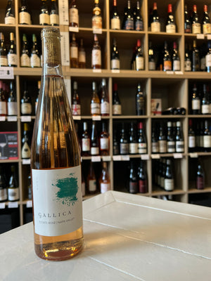 A tall, clear bottle of GALLICA ESTATE ROSÉ 2024 by WINE: JOHNSON BROS./OXFORD ST. gleams golden-pink with a white label and teal splash, topped by cork and gold foil, highlighting the wine’s refined style.