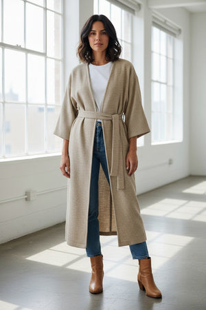 A woman poses against a plain light background wearing the MOMONI - CALL Lightweight Coat in Lurex Basketweave over a patterned shirt and loose, high-waisted beige wide-leg pants. She has straight dark hair and brown shoes.