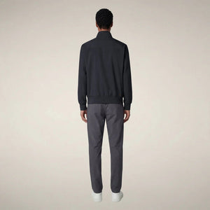 A person stands facing forward, wearing the SAVE THE DUCK - TULIO JACKET IN BLUE BLACK by SAVE THE DUCK, paired with gray pants and white sneakers, against a plain light background.