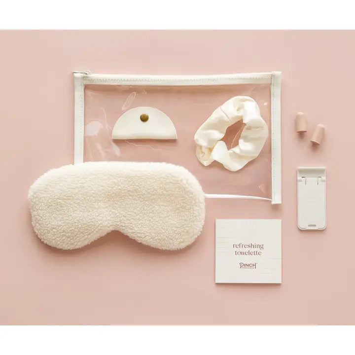 The PINCH PROVISIONS Travel Set is neatly presented in a transparent zippered pouch, designed for the contemporary traveler. Inside, you&#39;ll find a plush sleep mask, earplugs, cord organizer, phone/tablet stand, scrunchie, and a refreshing towelette. The packaging boasts a minimalistic design with &quot;PINCH PROVISIONS - TRAVEL SET&quot; and highlights the included 7 essentials.