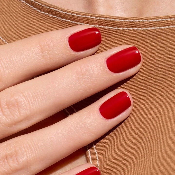 A close-up of the MANUCURIST - GREEN™ NAIL POLISH IN RED CHERRY brush, surrounded by glossy vegan polish from MANUCURIST INC, creating smooth ripples on the vibrant red surface.