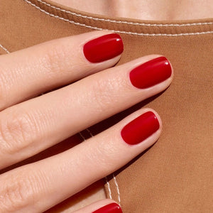 A close-up of the MANUCURIST - GREEN™ NAIL POLISH IN RED CHERRY brush, surrounded by glossy vegan polish from MANUCURIST INC, creating smooth ripples on the vibrant red surface.