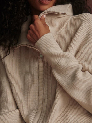 A person wearing a dark brown VARLEY - ENRICO ZIP-THROUGH KNIT JACKET featuring a ribbed soft viscose knit, a high collar, and a front zipper, ideal for cool weather layering.