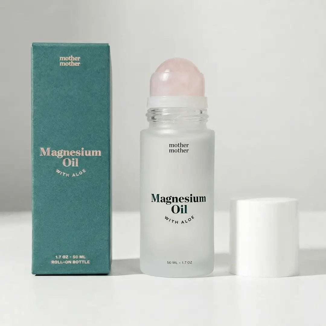 A green box and a frosted roll-on bottle of MOTHER MOTHER - MAGNESIUM OIL & ALOE ROLLER are displayed side by side. Designed for sensitive skin, the bottle from MOTHER MOTHER has its white cap removed and set to the right on a white surface.