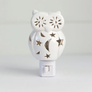 The OWL NIGHTLIGHT by LILY'S LIGHTS features a white ceramic owl design with cut-out star and moon patterns that allow light to shine through beautifully. Plugged into a white electrical base and set against a plain white background, this nightlight exemplifies quality craftsmanship, making it one of the most unique gifts.