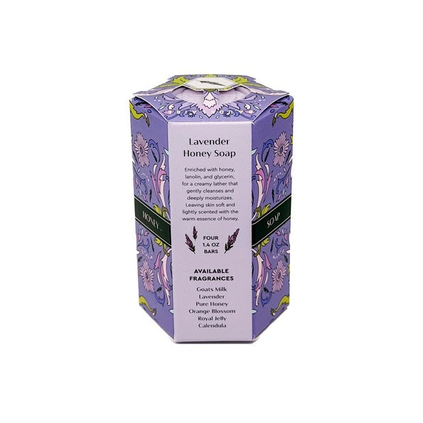 Four lavender soap bars are neatly stacked beside a purple box accented with floral designs and decorative yellow and green details, labeled “BAUDELAIRE - LAVENDER HONEY SOAP 1.4 OZ QUARTET.” From the BAUDELAIRE brand, these luxurious triple-milled soaps create a rich, creamy lather.