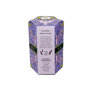 Four lavender soap bars are neatly stacked beside a purple box accented with floral designs and decorative yellow and green details, labeled “BAUDELAIRE - LAVENDER HONEY SOAP 1.4 OZ QUARTET.” From the BAUDELAIRE brand, these luxurious triple-milled soaps create a rich, creamy lather.