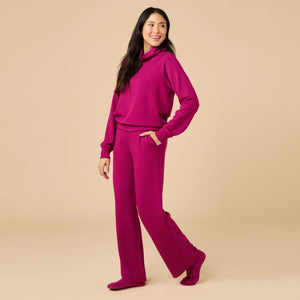 A woman seen from behind wearing the fuchsia SOFTIES - DREAMTECH COWL NECK WITH PLEATED PANT set featuring a long-sleeved cowl neck top and matching pleated pants.