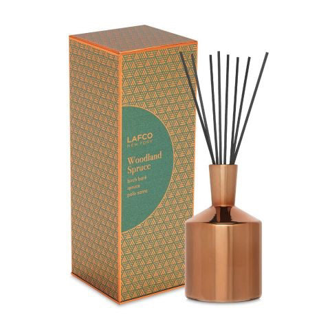A boxed LAFCO - WOODLAND SPRUCE DIFFUSER is displayed next to its bottle. The copper-colored bottle, with black reed sticks inserted, exudes the scent of spruce and birch bark. The box design features geometric patterns in green and gold with an orange border.