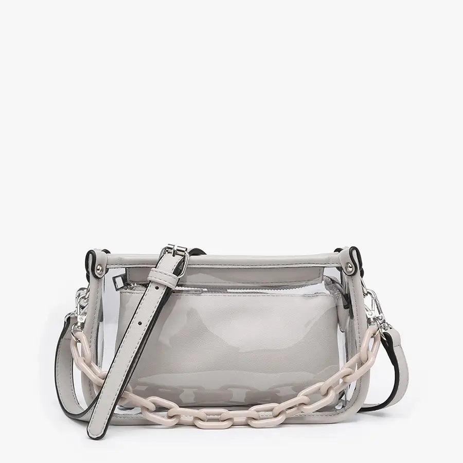 Introducing the CLEAR CROSSBODY BAG by JEN &amp; CO: A stylish handbag crafted from vegan leather, showcasing a layered beige design with an open top and a visible zipper pocket. This bag is elegantly framed by a transparent outer layer and is complemented by a chunky beige chain strap for additional style and versatility.