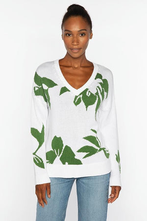 A woman faces forward wearing the KINROSS CASHMERE Intarsia Easy Vee Neck Cotton Sweater, featuring green leaf patterns. Her hair is up, and she pairs it with light blue jeans against a plain white background. 100% cotton by KINROSS.