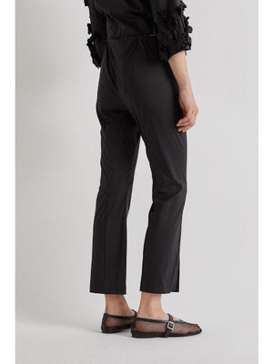 A person stands against a plain background wearing MEIMEIJ FROTN HEM SPLIT COTTON PANT—black, cropped, ankle-length pants with small slits. They also wear a black textured-sleeve top and black shoes. Their face is not visible in the image.