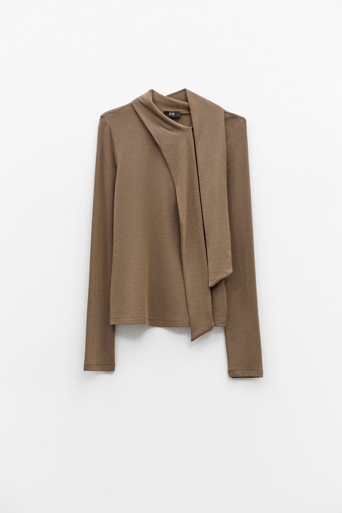 The ELEH - THE SCALA TIE-NECK TOP by ELEH is a light brown, long-sleeved minimalist blouse featuring an asymmetrical attached scarf draped across the front, shown on a hanger against a plain white background.