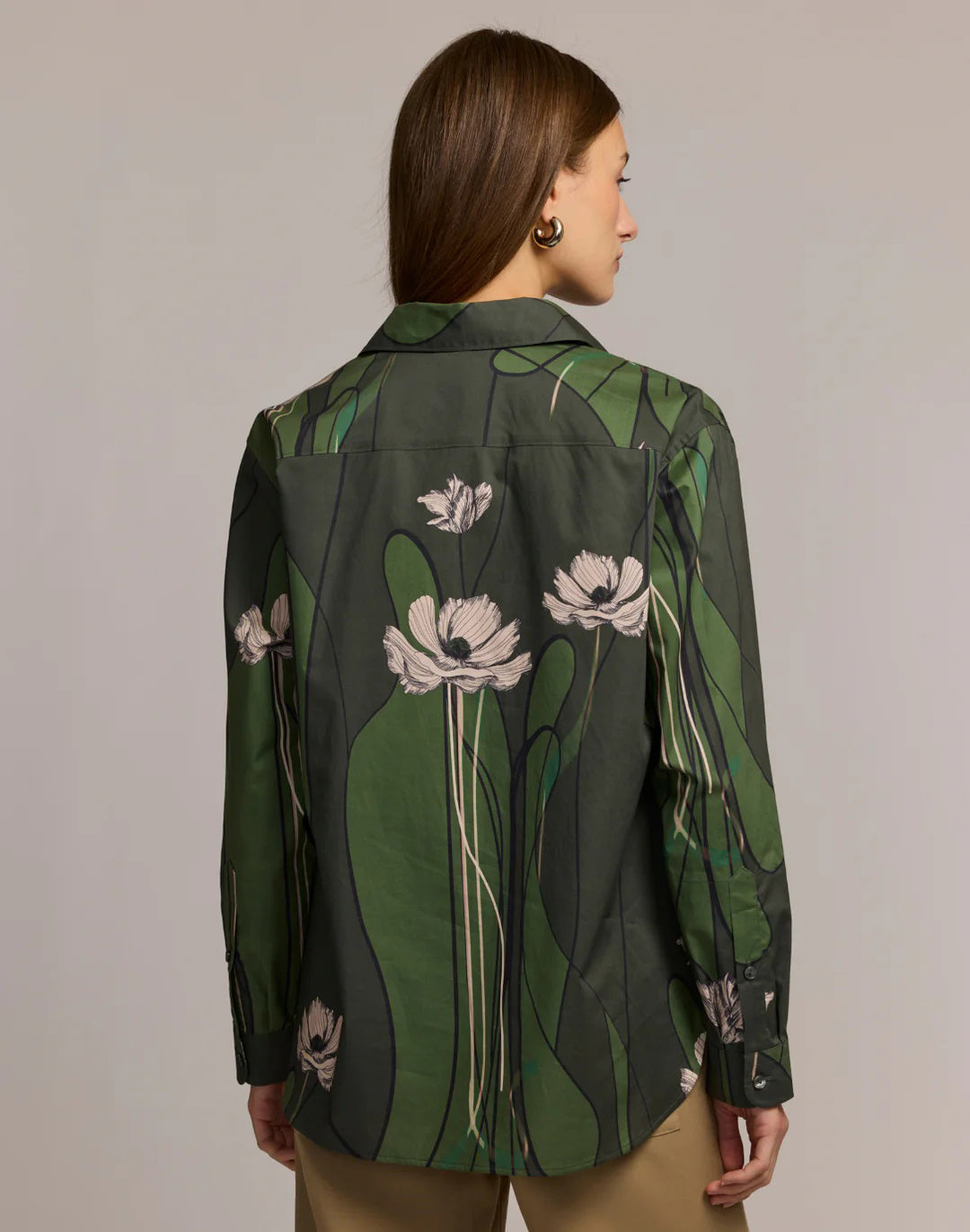 A woman with long brown hair wears the HINSON WU Halsey Long Sleeve Shirt in Poppy Print and tan pants, standing with her hands in her pockets against a neutral background.