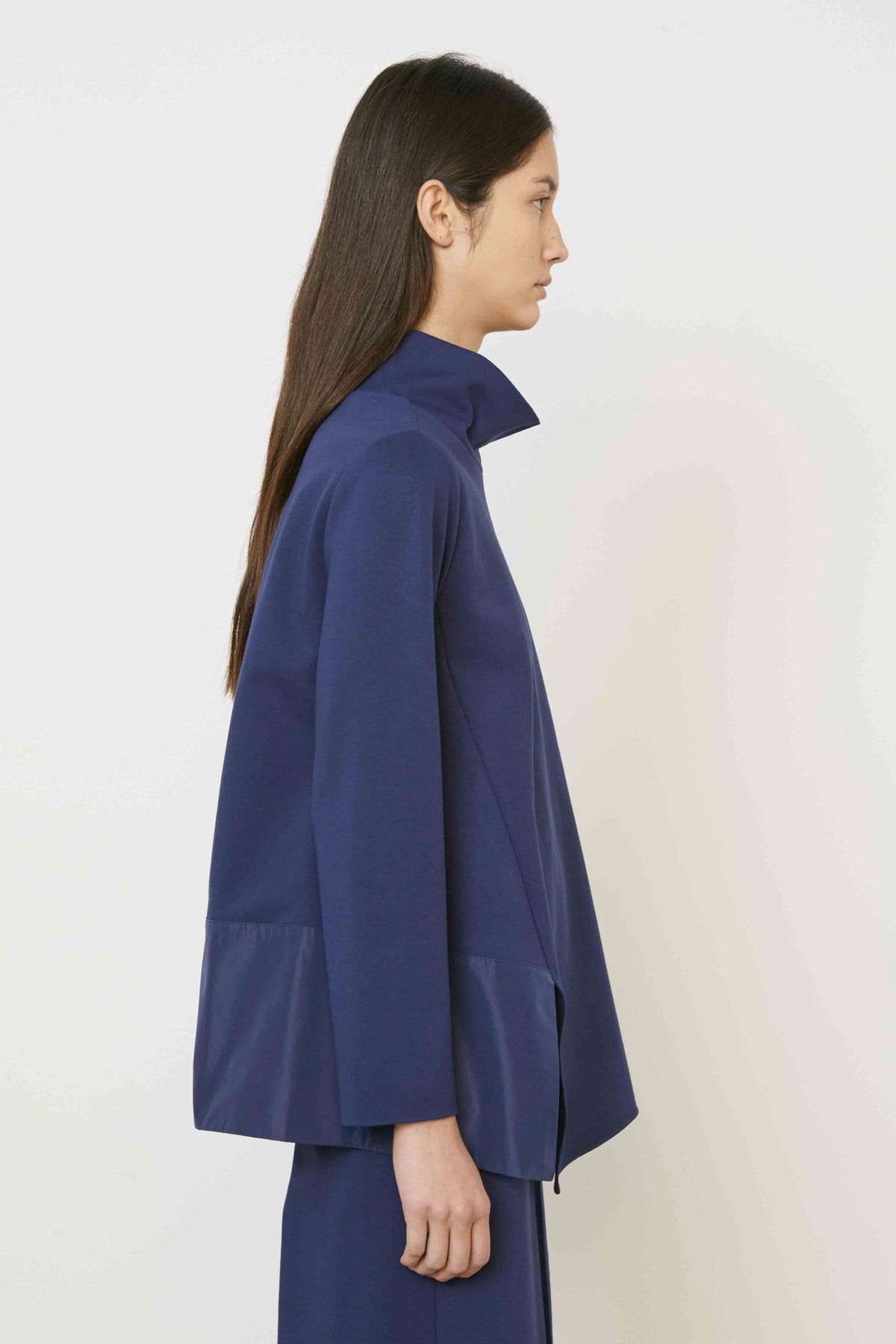 A woman with long brown hair, seen from behind, wears the MEIMEIJ Mixed Media Cowl Neck Top in dark blue with a shiny panel at the bottom and matching pants. She stands against a plain, light background.