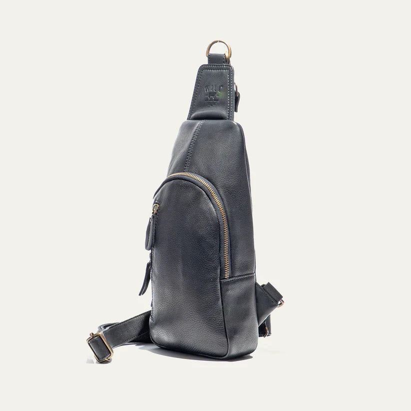 The WILL LEATHER GOODS - ZIP AROUND SLING BAG IN BLACK is a full-grain leather sling bag with gold zippers and buckle, small front pocket, adjustable strap, and top hanging loop, shown against a plain white background.