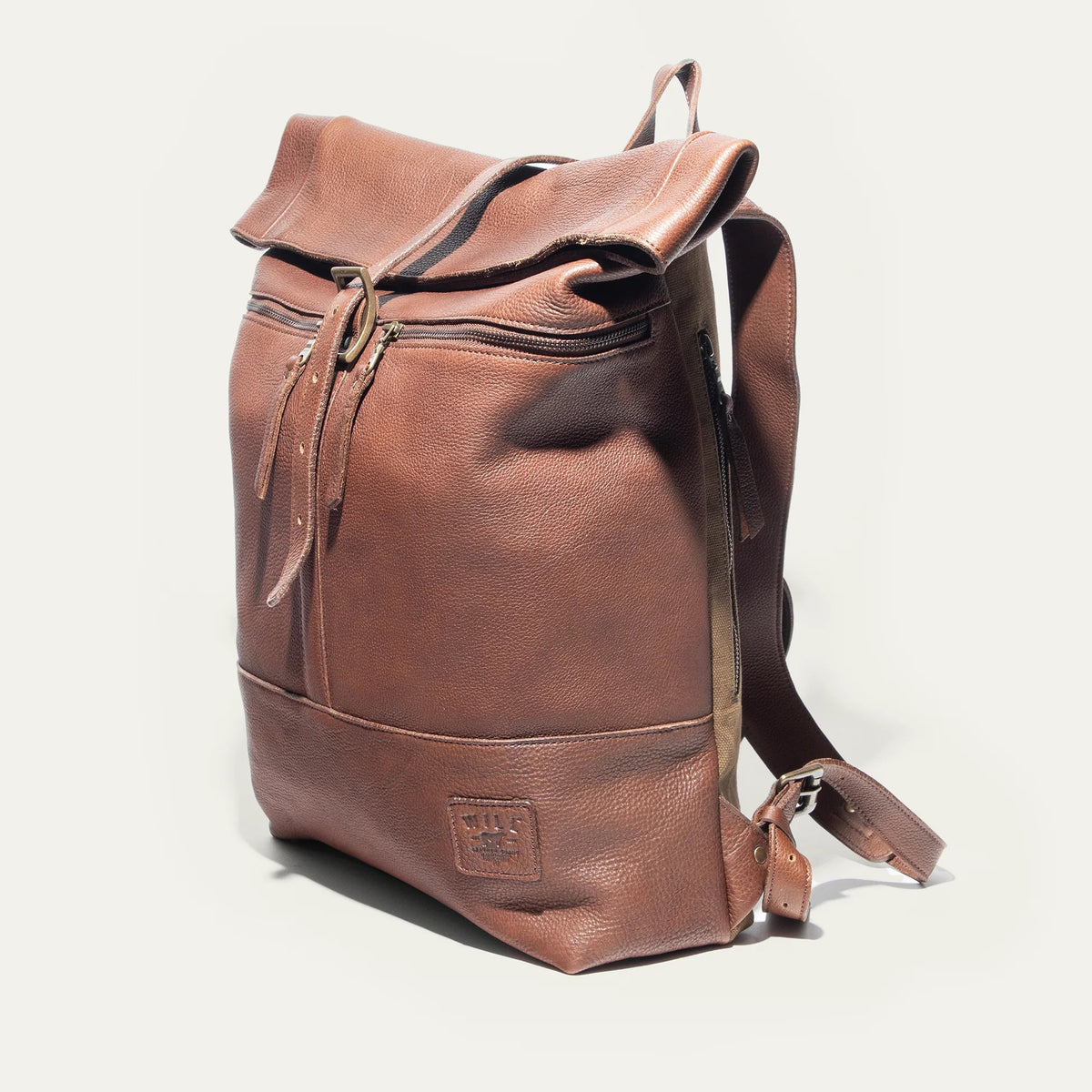 The WILL LEATHER GOODS - ROLL TOP BACKPACK by WILL LEATHER GOODS is open, showing a camera, a red-and-black plaid lining, an Andrzej Sapkowski book, and an old yellowed map inside.