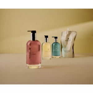 Four Molton Brown hand care products are lined up on a beige surface—three vibrant pump bottles with fresh coastal scents, plus one Coastal Cypress Hand Wash Refill 400ml silver pouch.