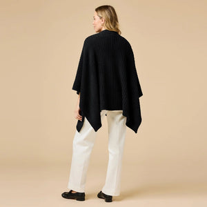 A woman wearing a black SOFTIES - SOLID RIB MARSHMALLOW SHAWL over a grey top and white trousers.