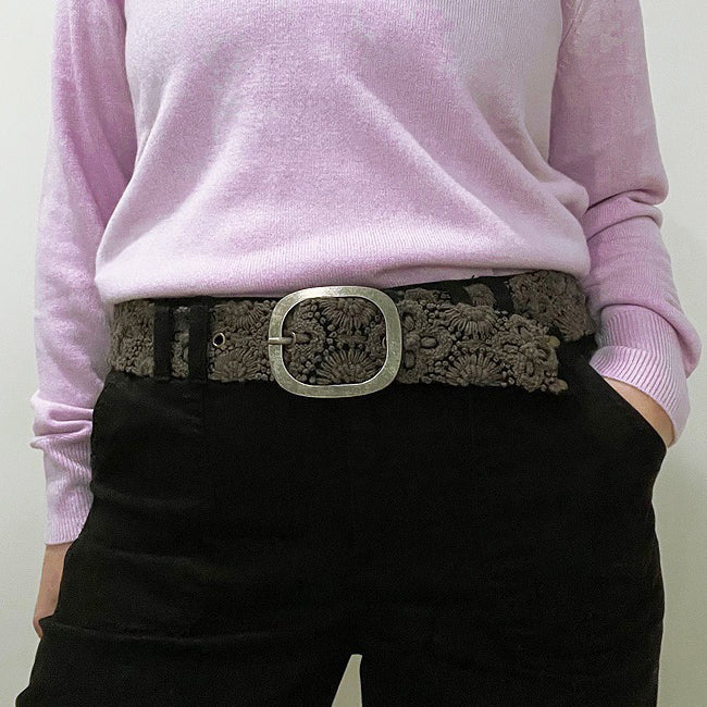 The JENNY KRAUSS - MIDNIGHT OASIS BELT features intricate raised floral embroidery, a round metal buckle, and a dark brown design, handcrafted in Peru and shown coiled on a light background.