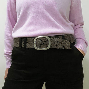 The JENNY KRAUSS - MIDNIGHT OASIS BELT features intricate raised floral embroidery, a round metal buckle, and a dark brown design, handcrafted in Peru and shown coiled on a light background.
