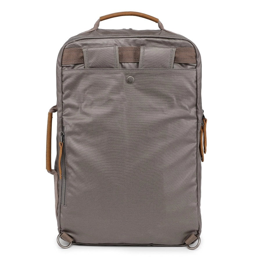 A close-up of the TSD BRAND - MADRONE Coated Canvas Backpack in Grey shows its brown leather accents and an unzipped front pocket with a black wallet partially visible inside.
