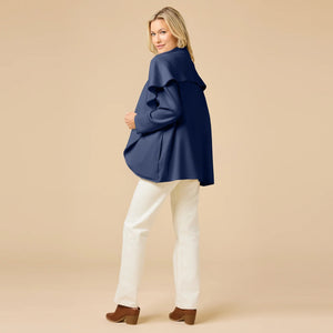 A woman wears an off-white SOFTIES - DREAMTECH EXAGGERATED COLLAR CARDIGAN with an exaggerated waterfall collar, cinched at the waist with a thin belt, and holds a matching handbag.