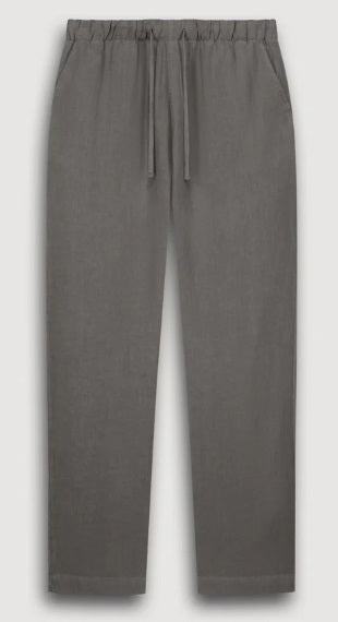 A man stands against a plain background wearing a light gray long-sleeve henley shirt, HARTFORD - LINEN JOGGY PANTS IN ARMY, and light-colored shoes, with his hands in his pockets.