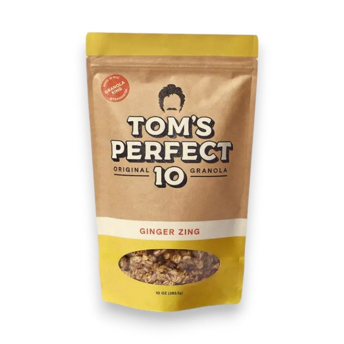 A brown and yellow pouch labeled "TOM'S PERFECT 10 - GINGER ZING GRANOLA" from TOM'S PERFECT 10, featuring a small window revealing maple syrup granola with candied ginger inside.