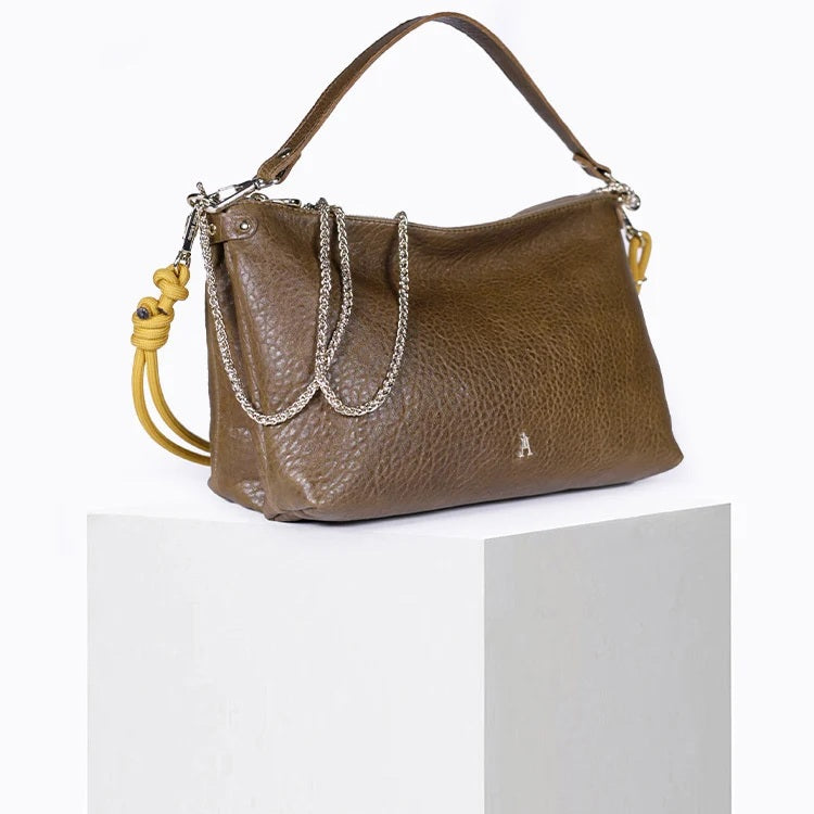 The CRAIE STUDIO - DUAL BUBBLE UMBER HANDBAG features brown bubble-textured leather, a gold zipper, and a chain strap. A large yellow knotted cord adorns one side for a unique decorative touch. The open bag reveals its interior and showcases the signature artistry of CRAIE STUDIO.