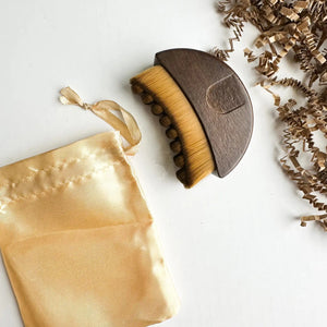 A SMILE BOUTIQUES LYMPHATIC BRUSH WITH NATURAL WOOD, featuring soft bristles, is displayed next to a satin drawstring pouch and brown paper packing material on a white surface. This elegantly designed facial massage brush is crafted from premium natural wood, making it a luxurious addition to your skincare routine.