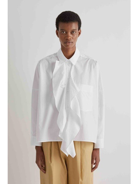 A person is facing away from the camera, wearing the MEIMEIJ - COTTON RUFFLE BLOUSE by MEIMEIJ with beige pants against a plain light background.