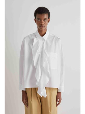 A person is facing away from the camera, wearing the MEIMEIJ - COTTON RUFFLE BLOUSE by MEIMEIJ with beige pants against a plain light background.